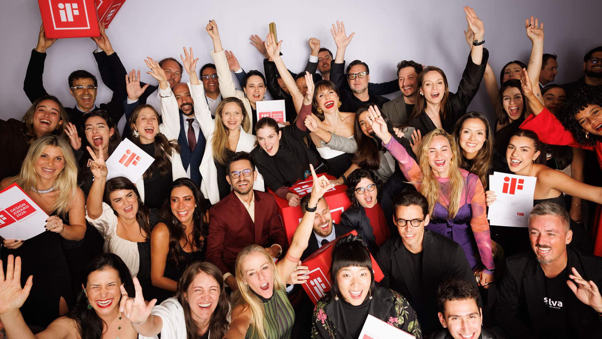 Vencedores do iF Design Award comemorando em grupo, com certificados vermelhos nas mãos
