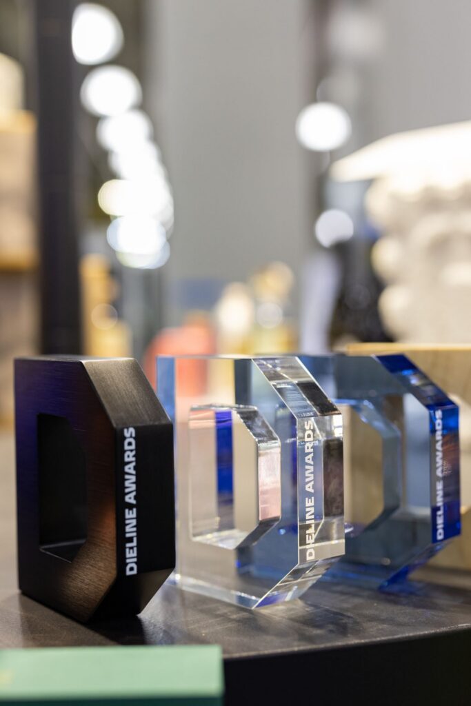 Três troféus do DIELINE Awards, em acrílico preto e transparente, sobre uma mesa