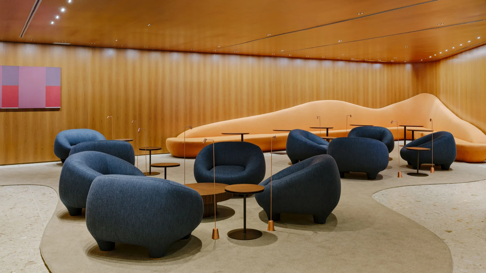 Sala de estar com paredes de madeira, poltronas azuis arredondadas e um sofá laranja longo em forma de montanha