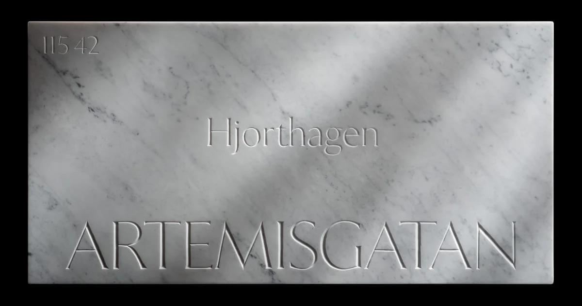 Placa de rua em mármore de Carrara com ARTEMISGATAN talhado em capitulares, o bairro Hjorthagen acima e o código postal 115 42 no canto