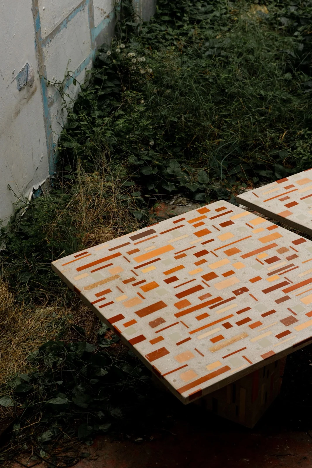 Close do tampo da mesa Dominó: retângulos de cerâmica laranja, terracota e creme embutidos numa massa clara e polida