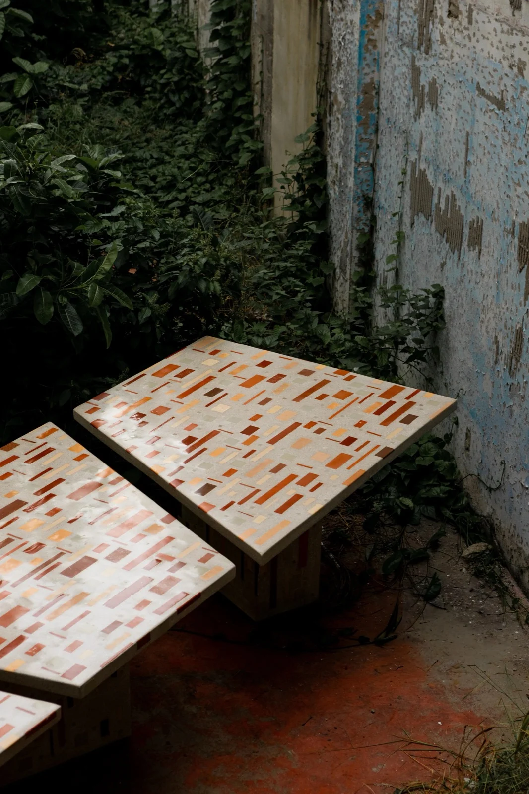 Dois módulos da mesa Dominó lado a lado, mostrando o tampo polido e a base quadrada revestida com o mesmo mosaico de cerâmica