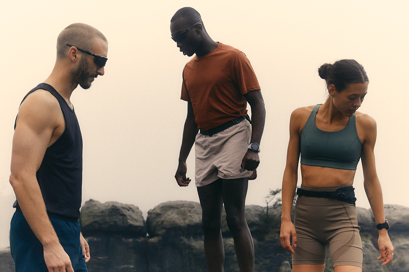 Três pessoas de roupa esportiva em tons de terra sobre pedras
