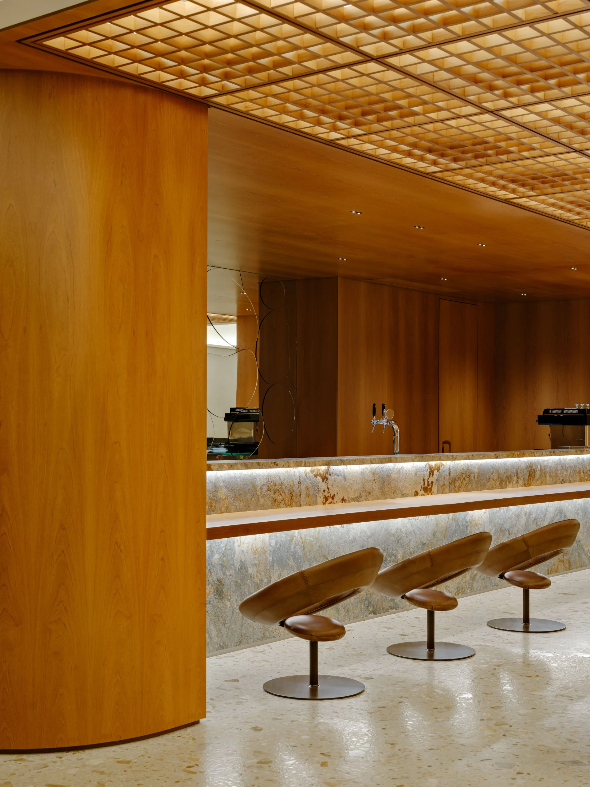 Bar Personnalité com pilar curvo de madeira, teto em grelha de madeira e bancos de couro diante do balcão de pedra