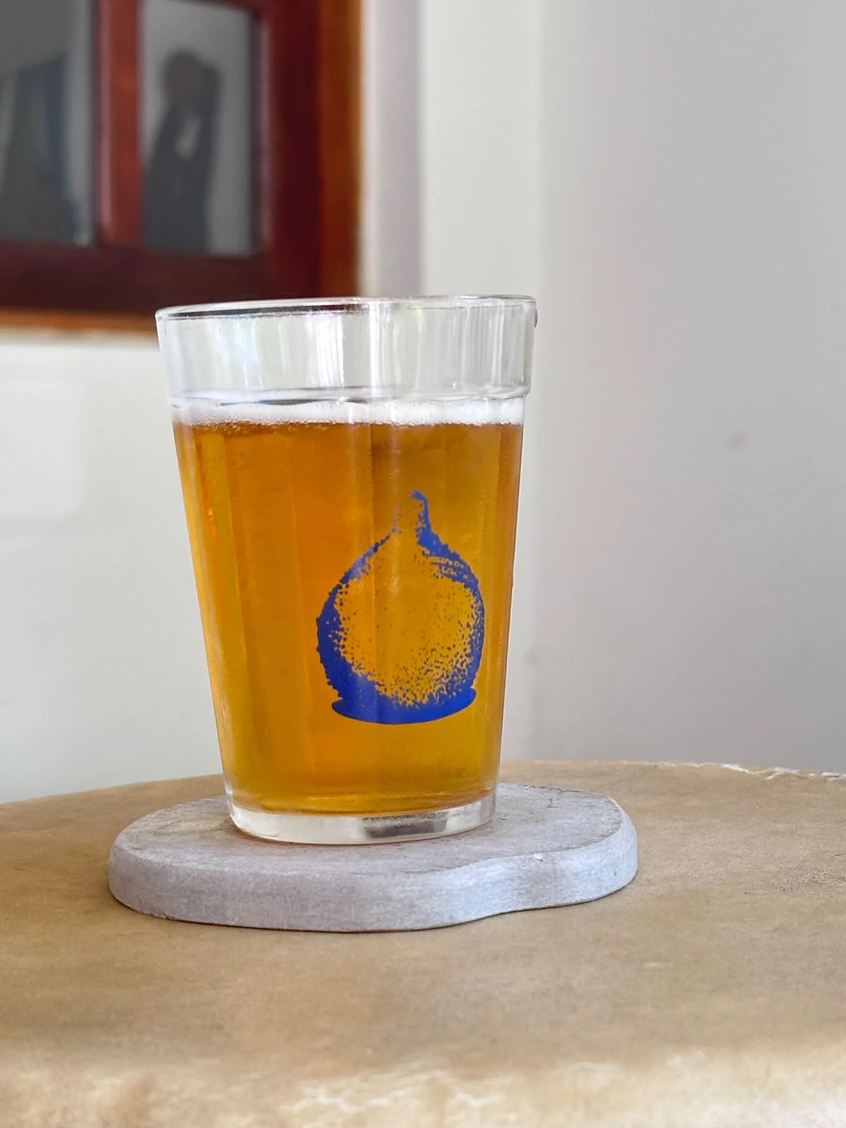 Copo americano com cerveja e um croquete pontilhado impresso em azul, sobre um porta-copos de pedra