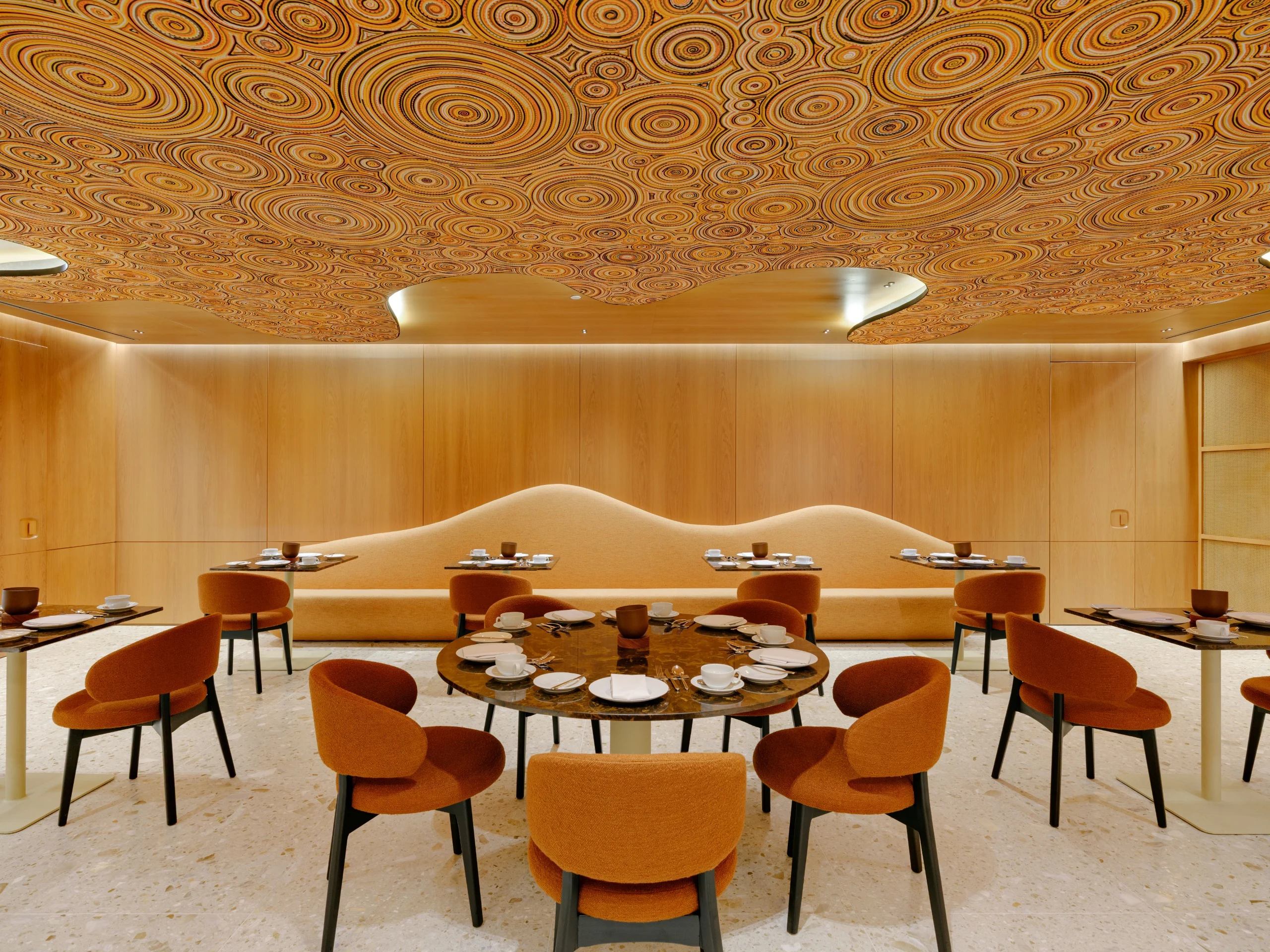 Restaurante da área Private com o teto coberto pela instalação Falésias, espirais em laranja, preto e dourado, e cadeiras laranja